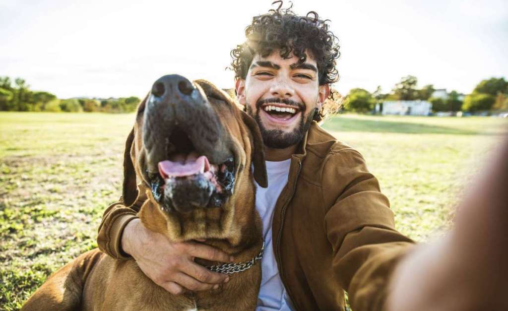 Young happy man taking selfie with his dog in a park - Smiling g